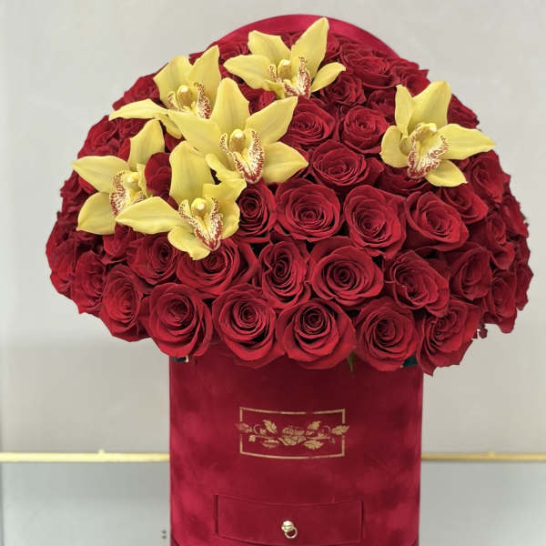 Round red hat box filled with red roses and topped with yellow orchids