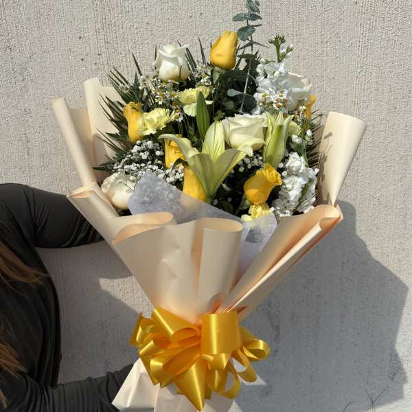 Bouquet of yellow and white flowers wrapped in beige paper with a yellow ribbon