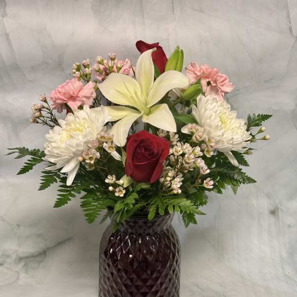Mixed bouquet with red roses, white lilies, and pink carnations in a dark vase