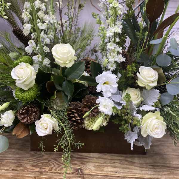 White roses and mixed flowers arranged in a wooden box with pinecones