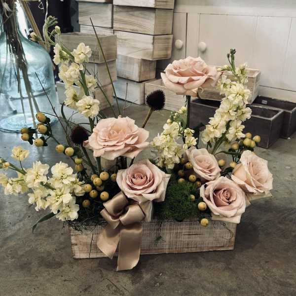Blush roses and cream flowers arranged in a wooden box with a satin ribbon.
