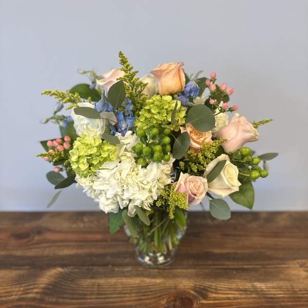 Mixed bouquet of white and green hydrangeas with peach roses and blue flowers in a glass vase