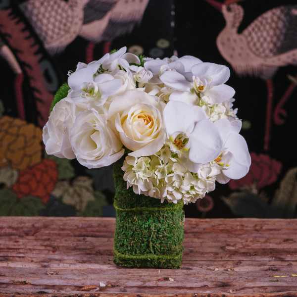 White roses and orchids arranged in a moss-covered vase