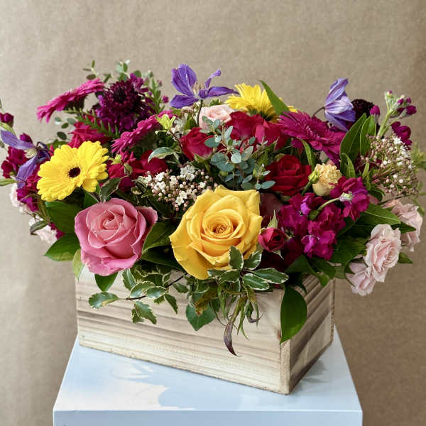 Mixed bouquet of roses, gerbera daisies, and purple blooms in a wooden box
