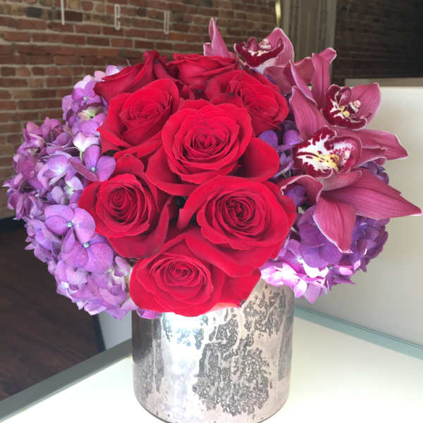 Red roses and purple orchids arranged in a silver vase