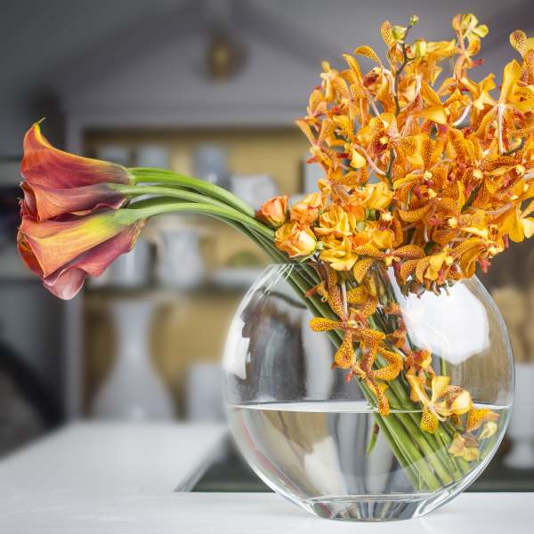 Orange orchids and calla lilies in a round glass vase
