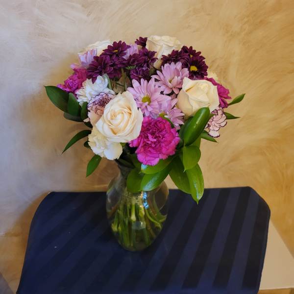 Mixed bouquet of white roses, pink daisies, and purple carnations in a glass vase