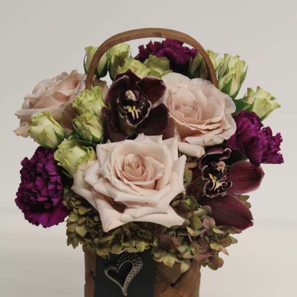 Tall woven basket arrangement with blush roses, purple orchids and carnations