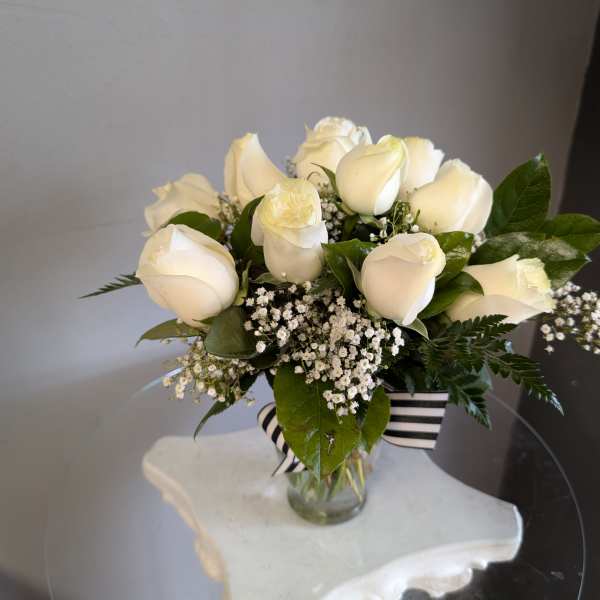 Compact arrangement of white roses and baby's breath in a clear vase with striped ribbon