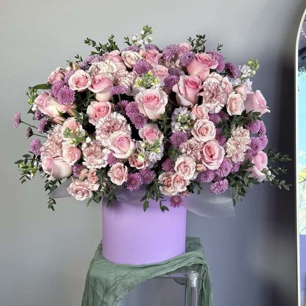 Large pink and lavender flower arrangement of roses and carnations in a lavender hat box container