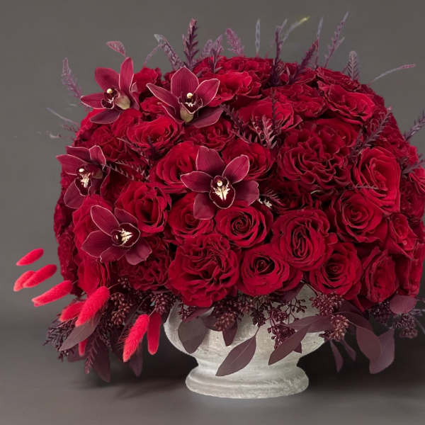 Red rose arrangement with dark orchids in a white pedestal vase