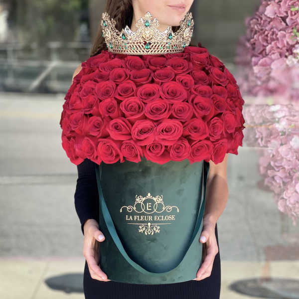 Woman holding a large box of red roses with a jeweled crown on top