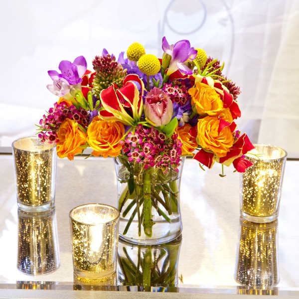 Colorful bouquet in a clear glass vase with gold candle holders