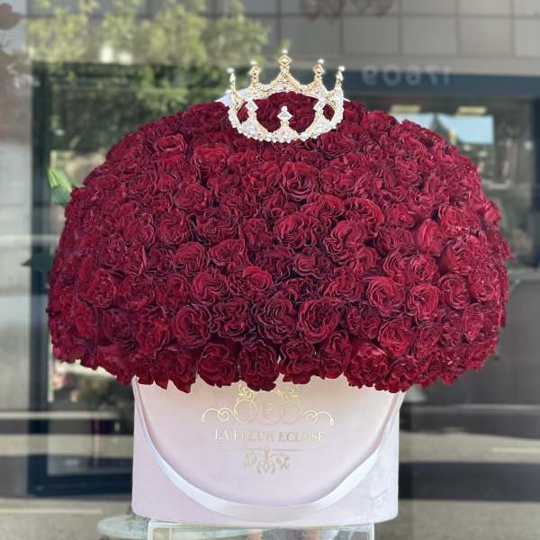 Large dome of red roses topped with a jeweled crown in a pink hatbox