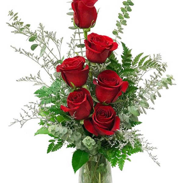 Red roses arranged in a clear glass vase with airy greenery