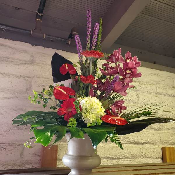Tall mixed floral arrangement in a white vase with red and purple blooms