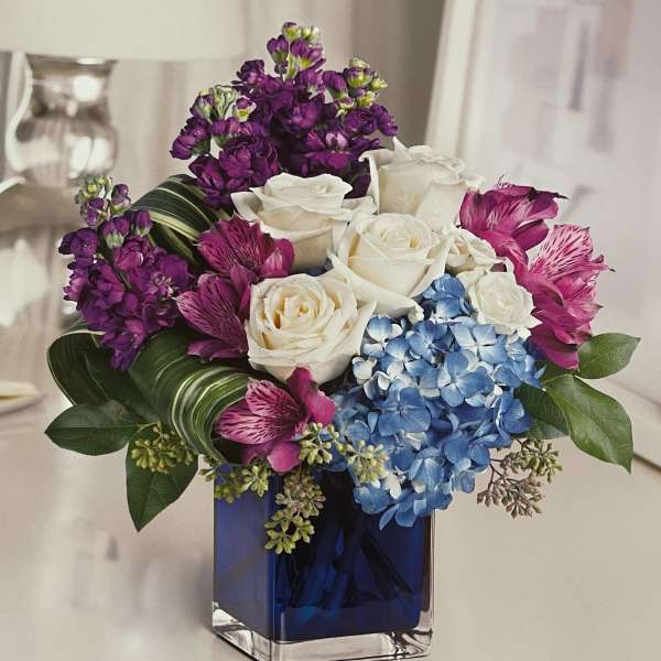 Bouquet of white roses, blue hydrangea, and purple flowers in a blue glass vase