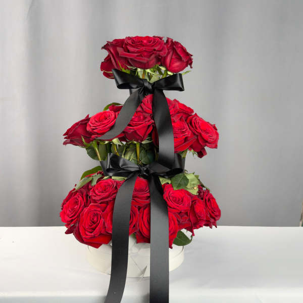 Tiered arrangement of red roses with black ribbon in a white box