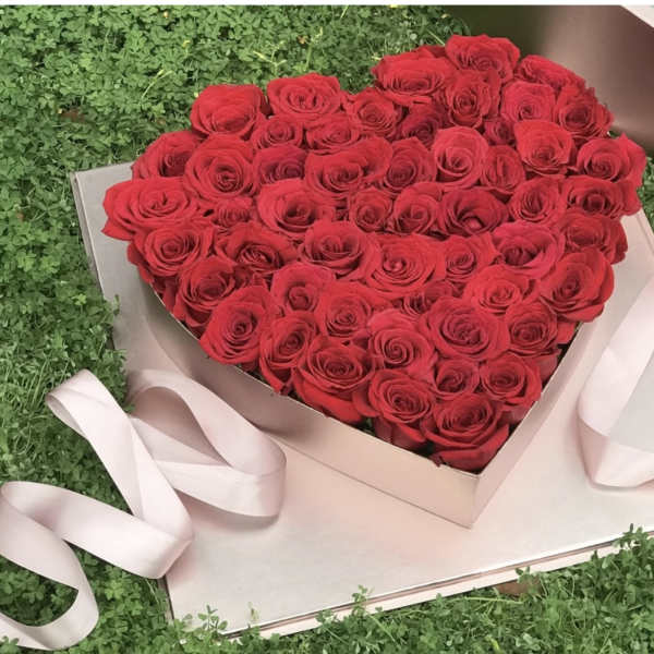 Heart-shaped box filled with red roses and pale pink ribbon