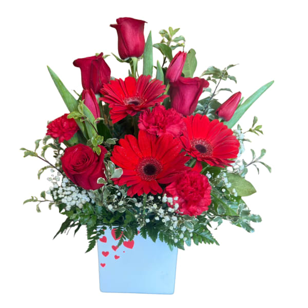 Red roses and gerbera daisies in a blue vase with heart accents