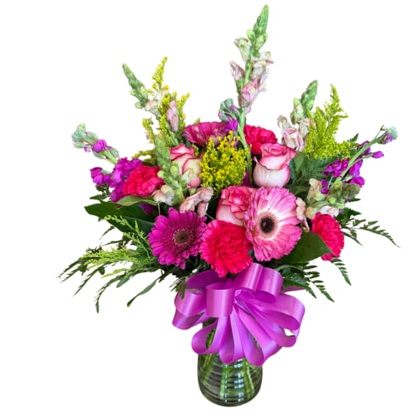 Bright pink and purple mixed flower arrangement in a green glass vase with a large purple bow