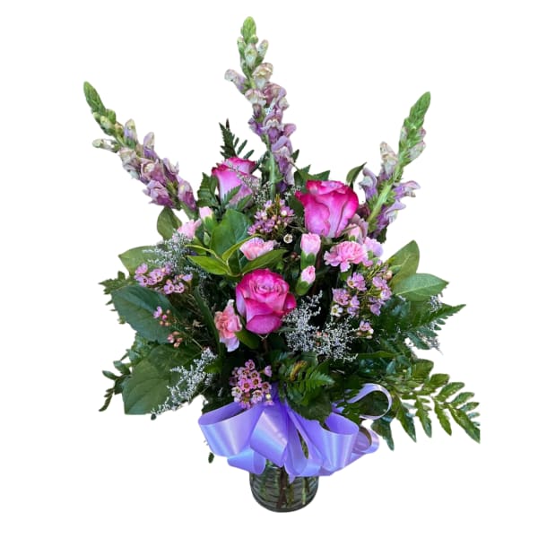 Mixed bouquet of pink roses, carnations, and tall snapdragons in a glass vase with a lavender ribbon bow.
