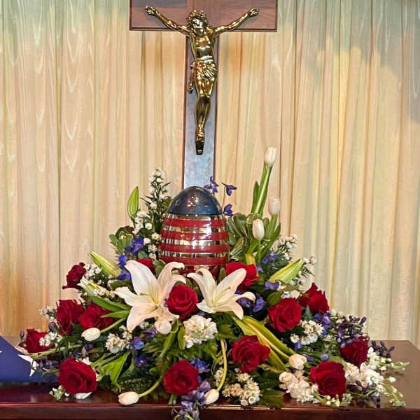 Red roses and white lilies arranged around a crucifix and patriotic egg centerpiece