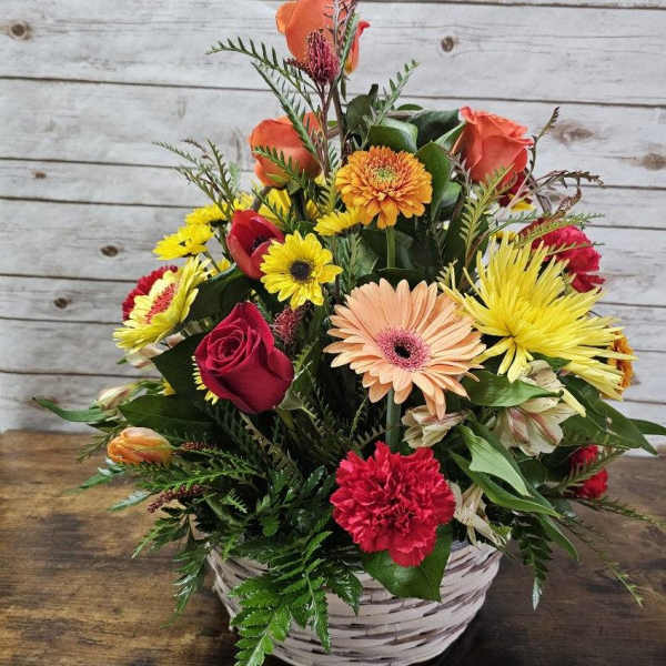 Bright mixed basket arrangement with red roses, orange gerberas, yellow daisies, and a red carnation