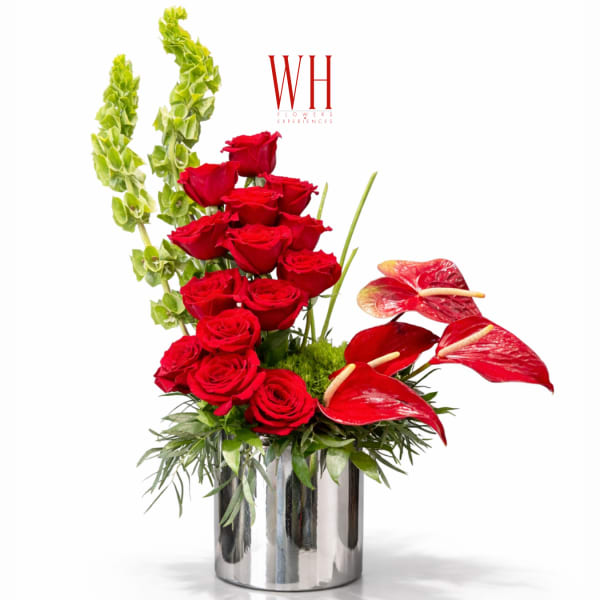 Red roses and red anthuriums in a silver vase with tall green spikes