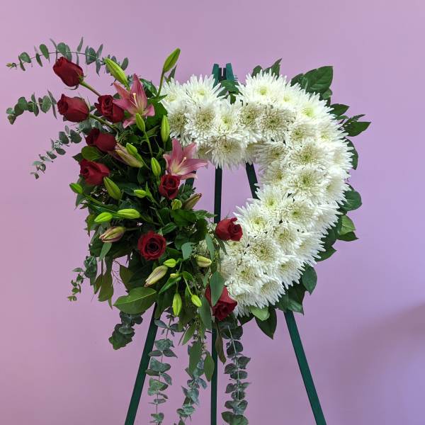 Heart-shaped floral wreath with white chrysanthemums and red roses on a stand
