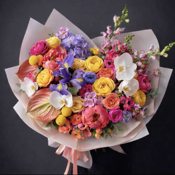 Colorful mixed bouquet with roses, orchids, and irises wrapped in pale paper