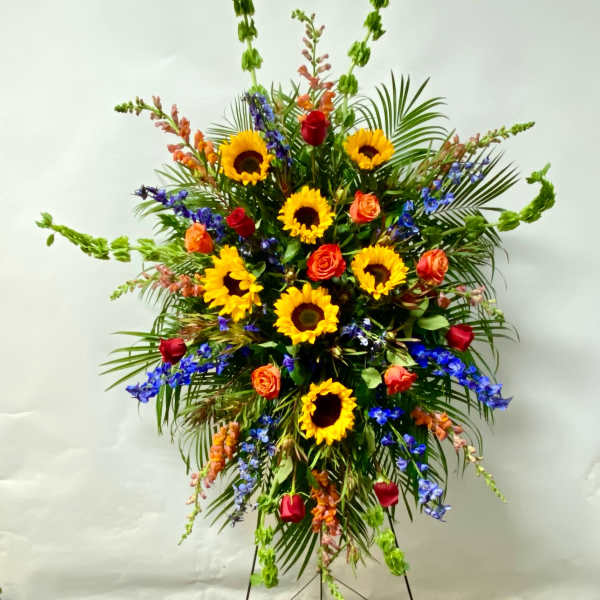 Tall standing floral spray with sunflowers, roses, and blue flowers