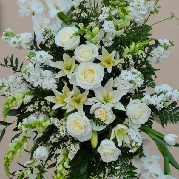 White floral standing spray with roses and lilies on a black easel