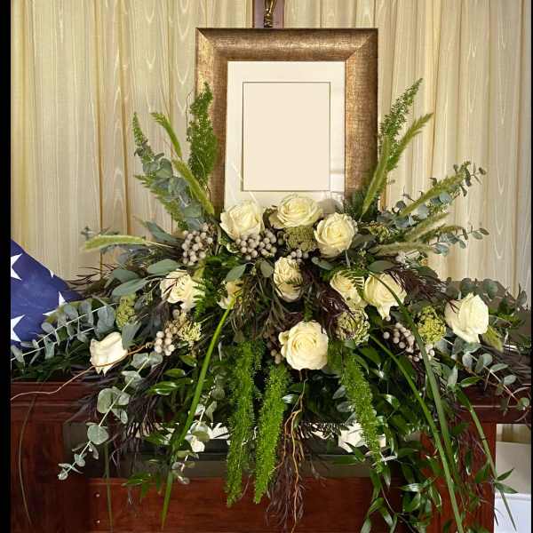 White rose funeral spray with cascading greenery in front of a framed display
