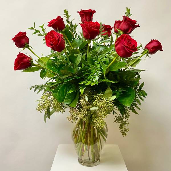 Red roses arranged in a clear glass vase with mixed greenery