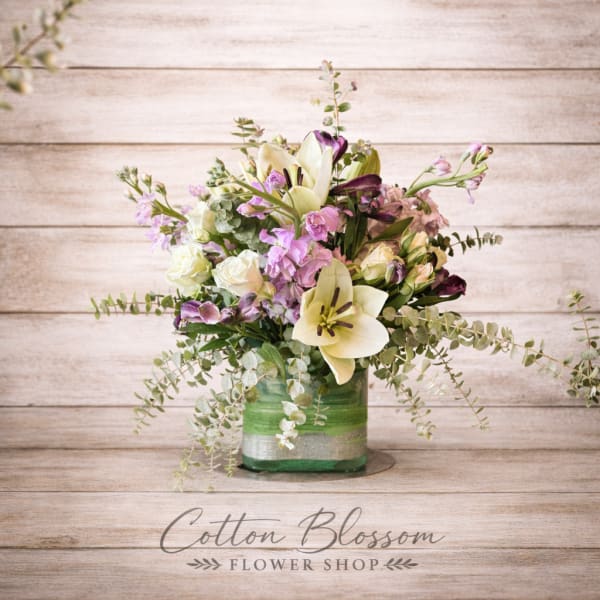 Mixed bouquet in a green glass vase with lilies, roses, and purple blooms