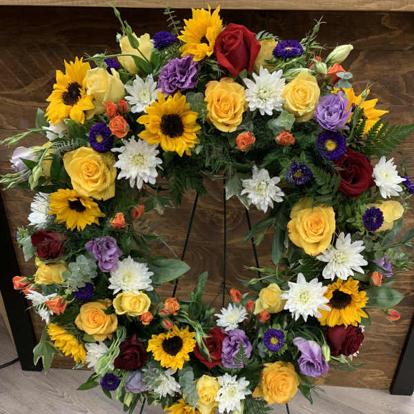 Heart-shaped floral wreath with roses, sunflowers, and white daisies on a stand
