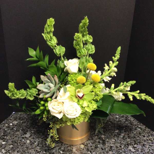 Green and white floral arrangement in a gold container