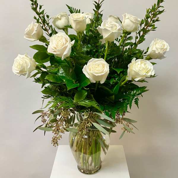 White roses arranged in a clear glass vase with mixed greenery