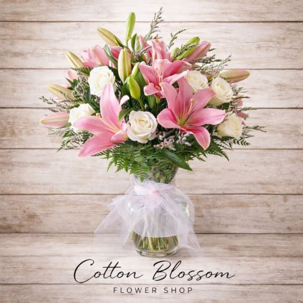 Pink lilies and white roses in a glass vase with a sheer ribbon