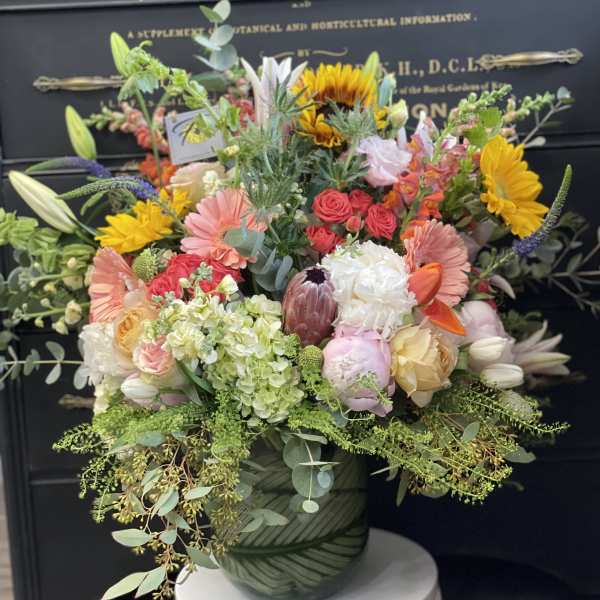 Mixed bouquet in a green patterned vase with sunflowers, roses, and lilies