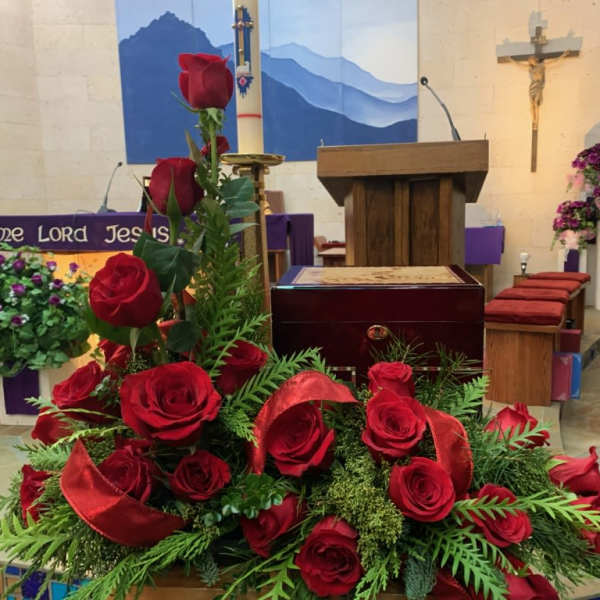 Red roses arranged in a church setting with red ribbon accents