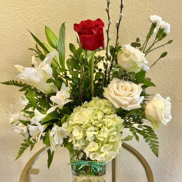 Mixed bouquet with red and white roses, lilies, and pale hydrangea in a glass vase