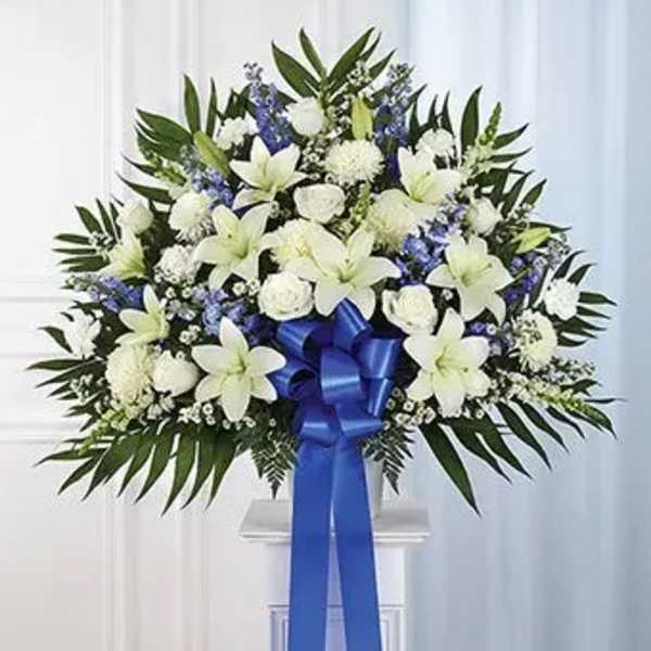 White lilies and blue flowers in a standing arrangement with a blue ribbon