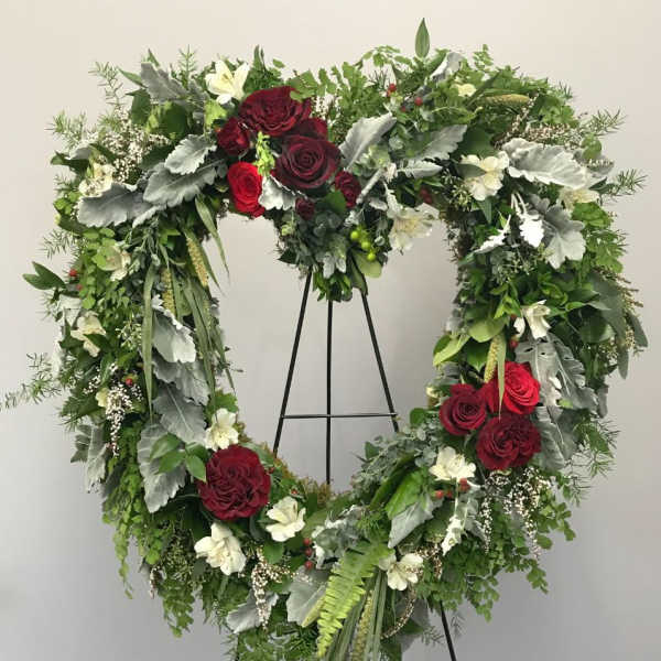 Heart-shaped floral wreath with red roses and white flowers on a stand