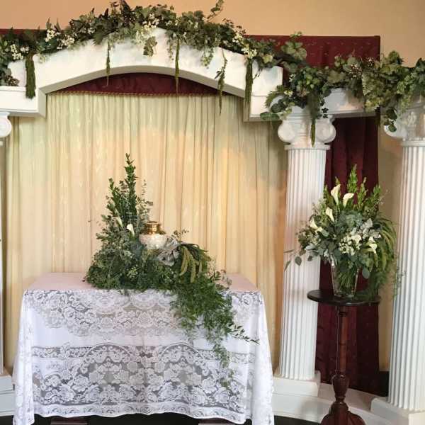 Floral altar display with white flowers and greenery on columns and a table