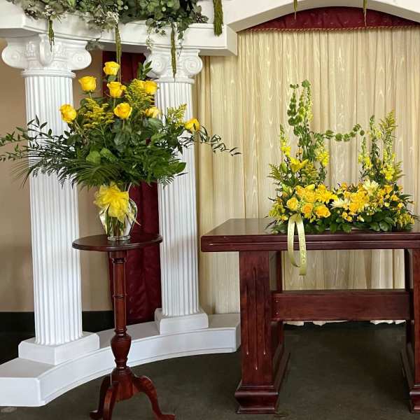 Yellow rose arrangements on pedestals around a wooden table