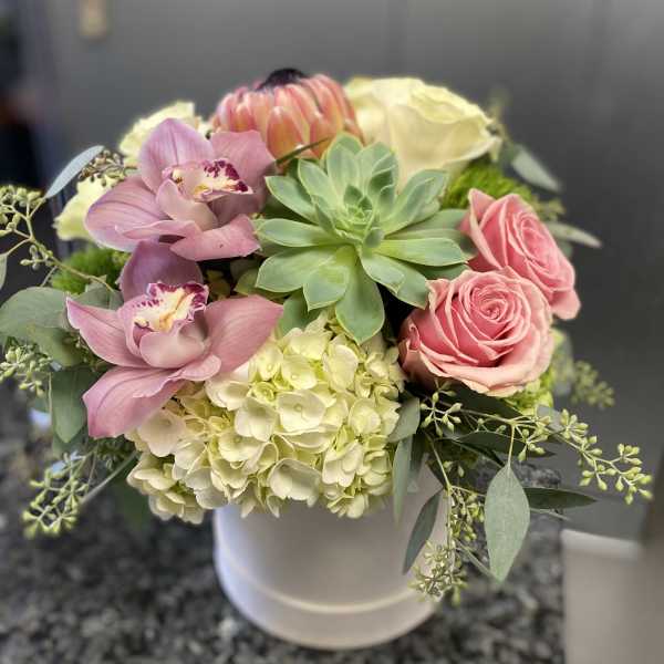 Pink orchids, roses, hydrangea, and a succulent in a white vase