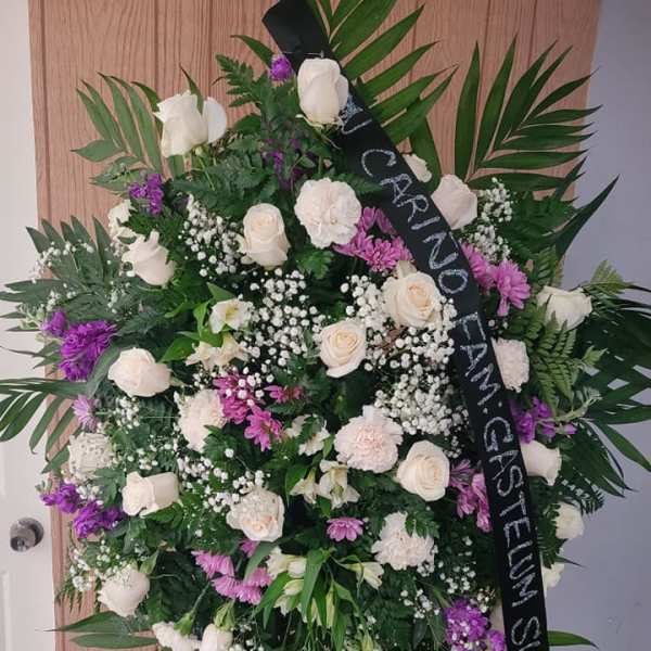Standing funeral wreath of white and purple flowers with a black memorial ribbon