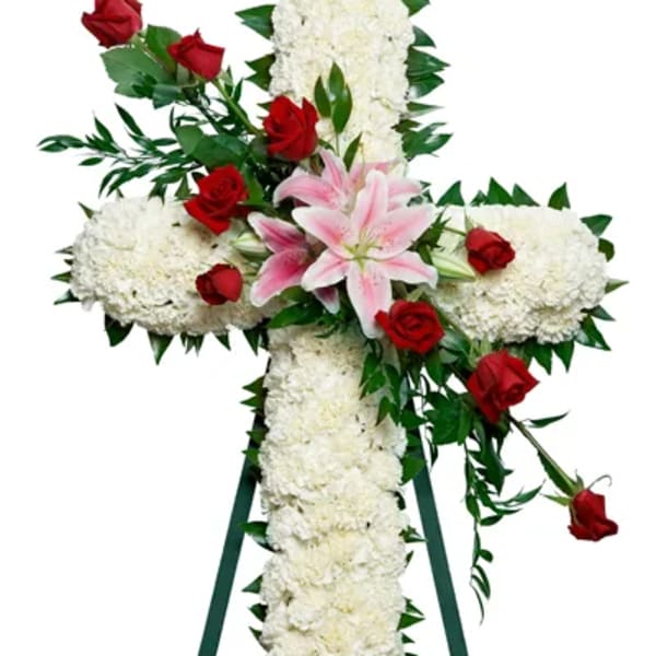 Cross-shaped floral tribute with white blooms, red roses, and pink lilies on an easel